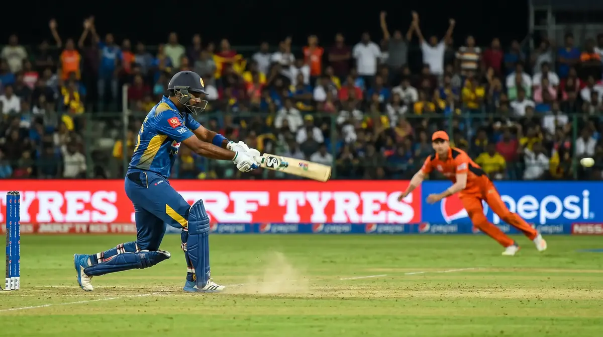 Cricket batsman playing a cover drive during a T20 match at a sunlit ground