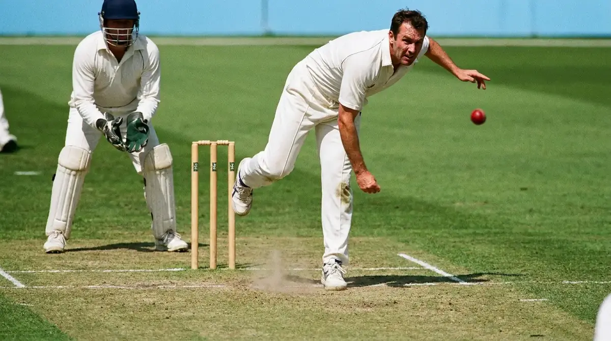 Cricket bowler delivering the first ball of a match with fielders positioned in a slip cordon