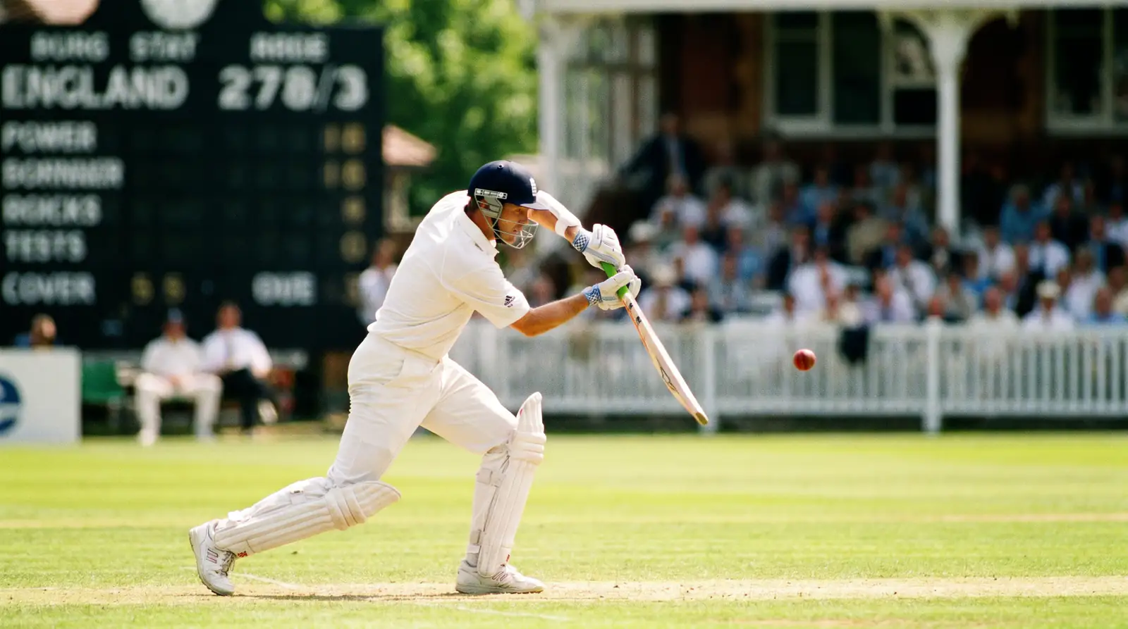 Cricket batsman playing a cover drive in a Test match with the scoreboard behind